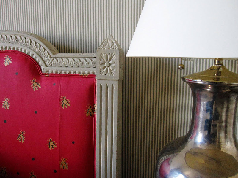 Detail of a bedroom in the Wedding Cake House in New Orleans with a Louis style headboard upholstered in a red, gold and black "bee" patterned fabric and striped upholstered walls