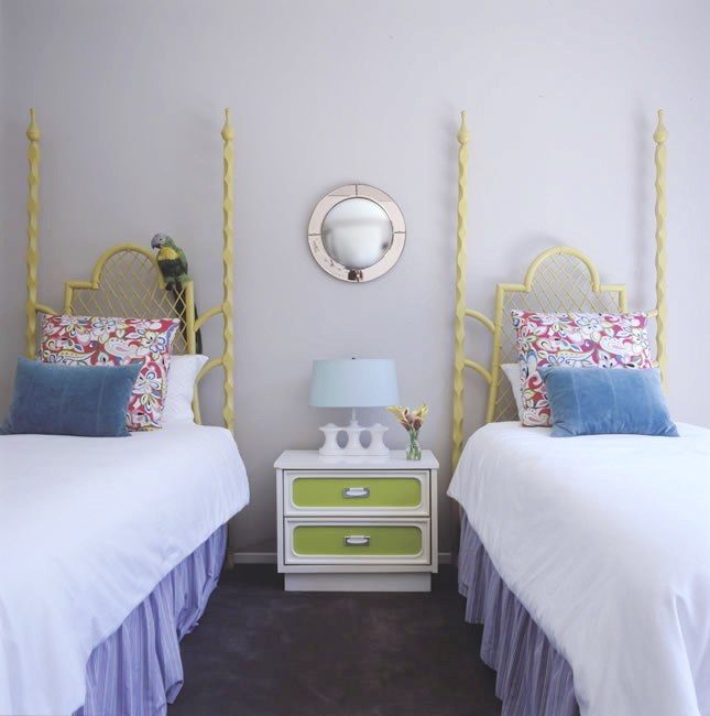 Children's bedroom with two twin beds with lime green spindle headboards, light purple walls, carpeted floor and a white nightstand with lime green drawers
