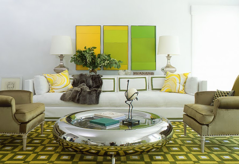 Modern living room with green dueling armchairs, a chrome donut-like coffee table, graphic green rug and a white sofa with green and yellow accent pillows