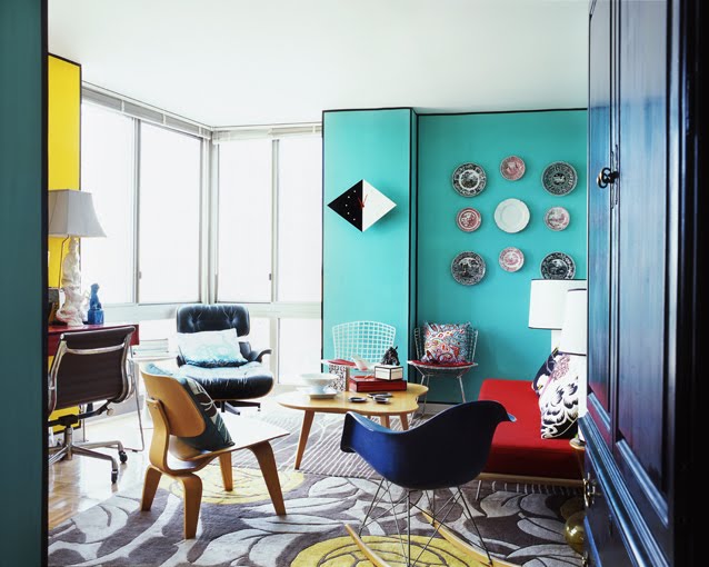 Conteporary living room with patterned rugs, a red sofa, blue Eames chair and turquoise walls with decorative plates