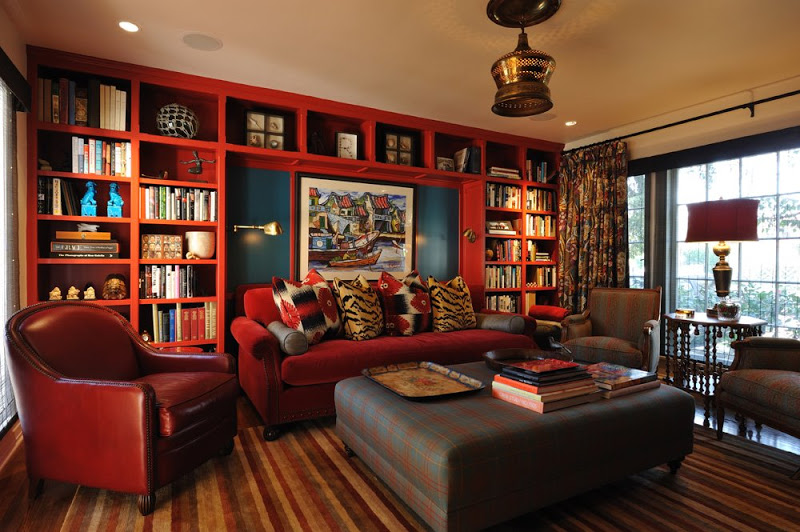 Television room in a Newman & Wolen designed home with red built in bookshelves, leather armchair with nailhead trim, red sofa, plaid armchair, stripped wood floor and an oversized plaid ottoman