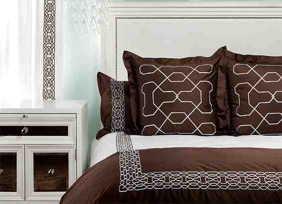 Bed with white headboard with nail head trim, brown pillows with silver embroidery and matching white and brown bedding