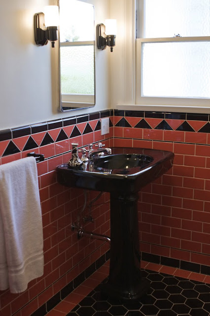 Guest bathroom with coral subway tiles on the wall, large black hexagon tile floor and a black pedestal sink