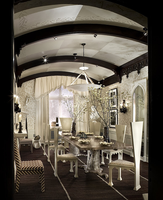 Gothic inspired dining room with vaulted ceilings and dark wood beams with modern dining tables and whimsical wallpaper, a giant glass mirror and framed photos of characters from Alice in Wonderland