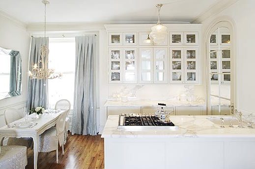 White kitchen by Kelly Giesen with white marble countertops, mirrored paned kitchen cabinets, a traditional dining table and chair and pale blue drapes