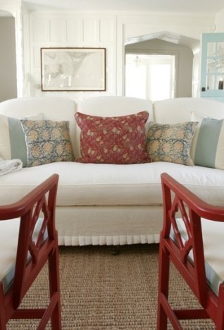 beach house living room with red Chippendale armchairs, a classic white sofa, and white paneled walls