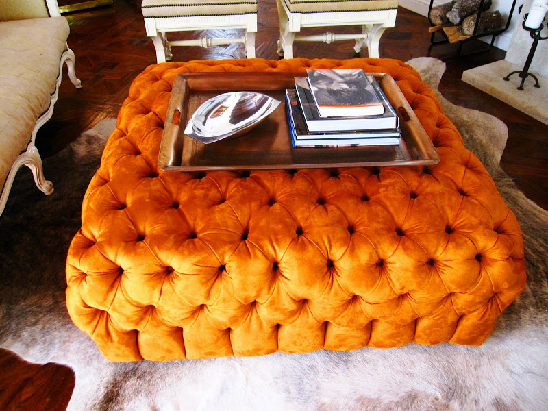 Orange suede tufted ottoman on a white animal skin rug in an LA living room