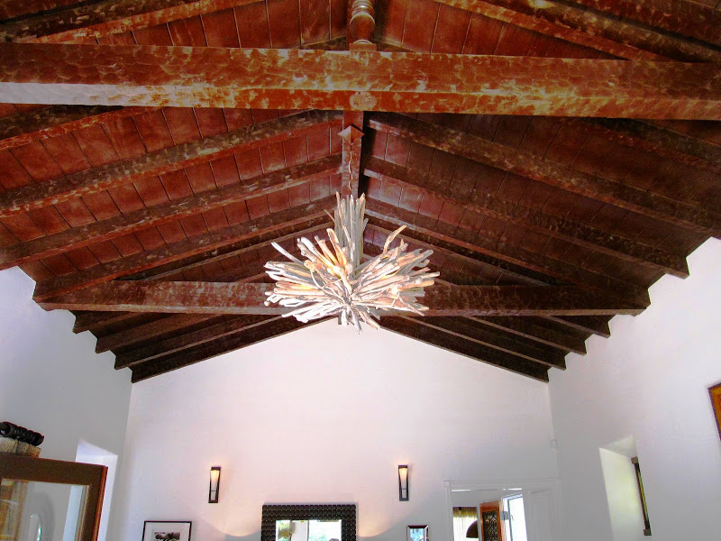 Vaulted ceiling with exposed wood beams and a simple chandelier made of tree branches in an LA living room