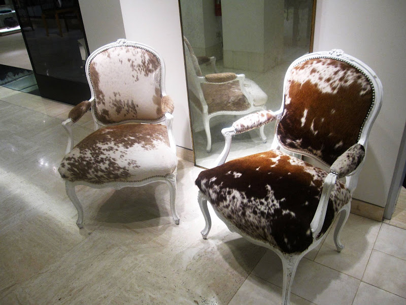 A pair of brown and white cow hide upholstered Louis XV bergeres with nailhead trim and glossy white lacquer paint in Neiman Marcus