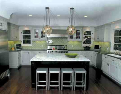 Kitchen with white cabinets, black counters, green subway tile backsplash, dark wood island with a white marble countertop, stainless appliances and multifaceted pendant lights