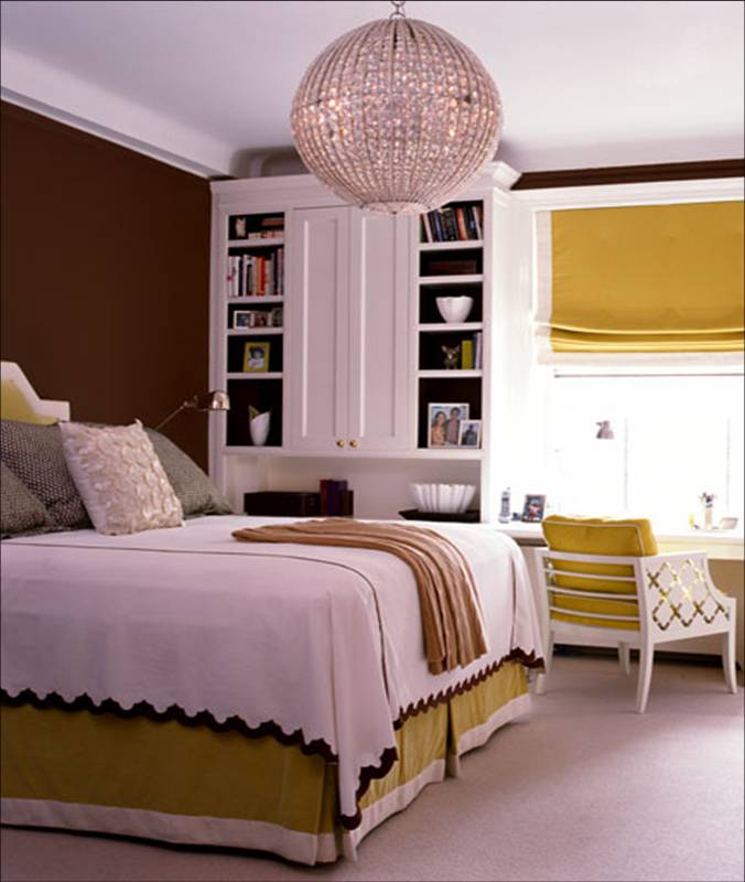 Bedroom with chocolate brown walls, yellow Roman shades, carved white lacquer accent chairs, yellow and white upholstered headboard and a large round chandelier by Amanda Nisbet