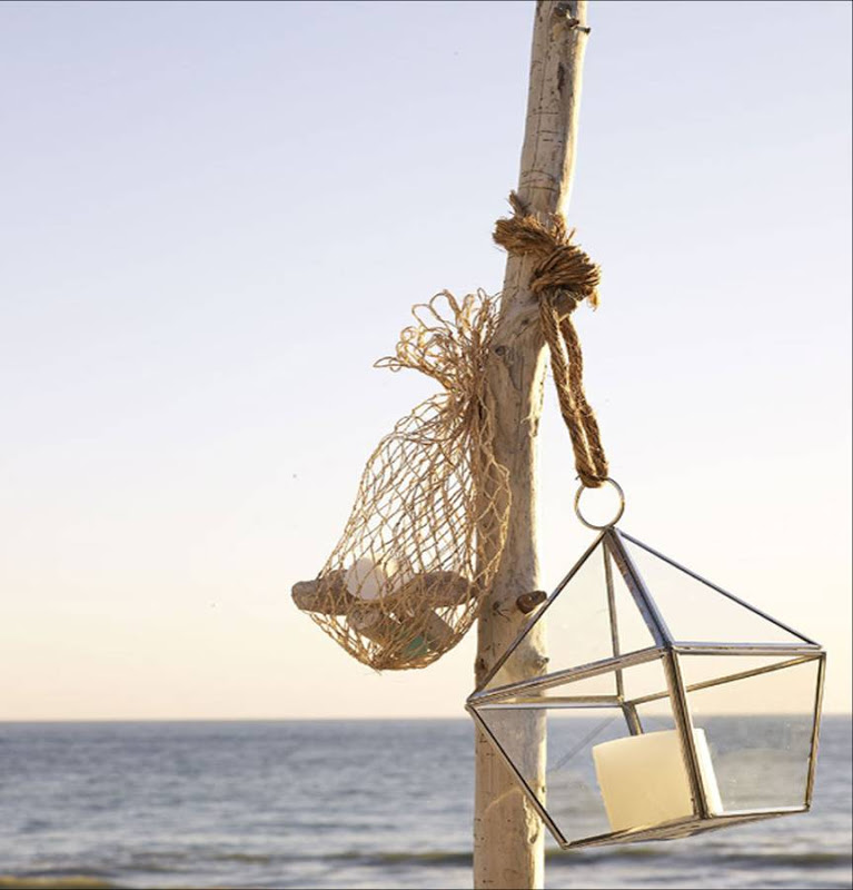 Reclaimed drift wood holds a glass lantern and a bag of small rocks on a deck overlooking the ocean by Sang An