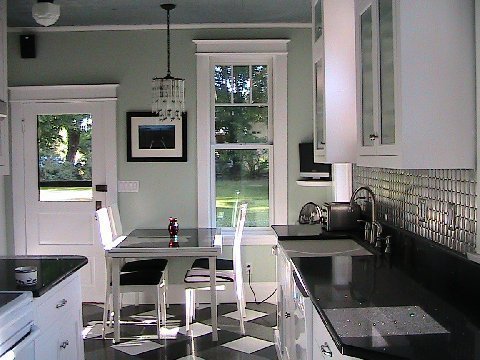 Mint kitchen after remodeling with black, grey and white tile floor, black countertop, Diamond Tech-Metal Series Mosaic Octagon Dots pattern backsplash, white cabinets and a crystal chandelier