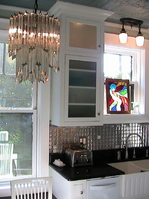 Kitchen after remodeling with a crystal chandelier, Diamond Tech-Metal Series Mosaic Octagon Dots tile backsplash, black counters, white cabinets and a stained glass accent piece 