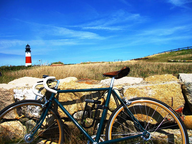 Bike leaning against a stone wall in Nantucket with a red and white lighthouse in the distance