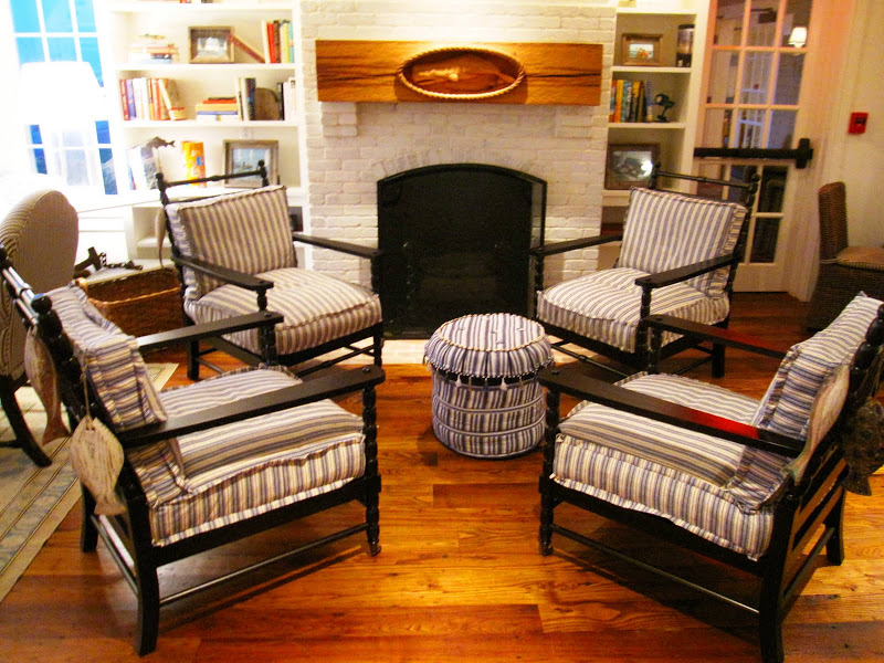 White painted brick fireplace with four wood slatted chairs with turned legs and blue and white seat cushions around a blue and white ottoman at the Great Harbor Yacht Club