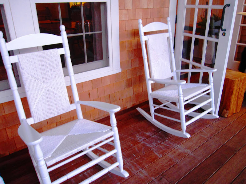 White rocking chairs sit on a wood porch overlooking the Nantucket Harbo