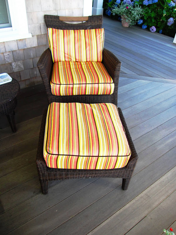 Dark brown wicker all weather armchair and ottoman with orange, yellow and brown striped cushions on a front porch in Nantucket