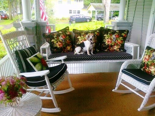 White rocking chairs flank a white wicker sofa with blue and white cushions, flower accent pillows and a beagle