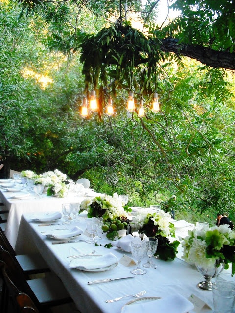 Custom vintage inspired outdoor chandelier hangs over a two long tables at an outdoor wedding