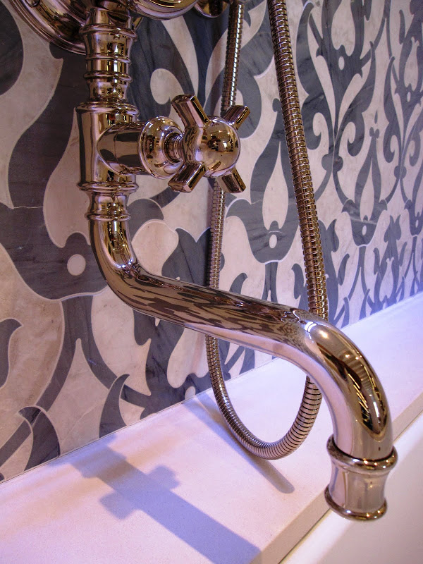 Polished metal faucet and shower spout on a marble mosaic tile wall inside Waterworks