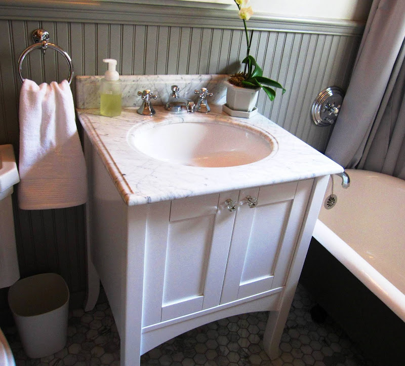 White wood vanity cabinet in a bathroom by Newman & Wolen Design with hexagon marble mosaic tile floor, claw foot tub and grey wainscoting