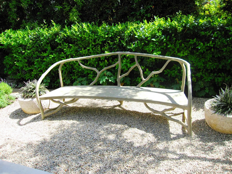 Faux bois bench with a curved back and twig design in a garden with a lily pond