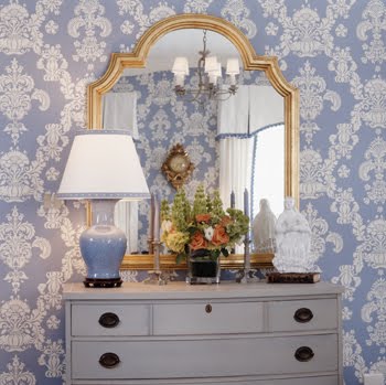 Blue bedroom with damask wallpaper, periwinkle porcelain lamp and a gold mirror above a white chest of drawers by Kelley Proxmire