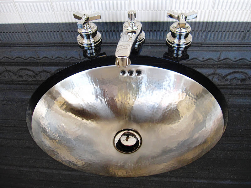 Bathroom with pounded copper oval sink with nickel finish and black countertop