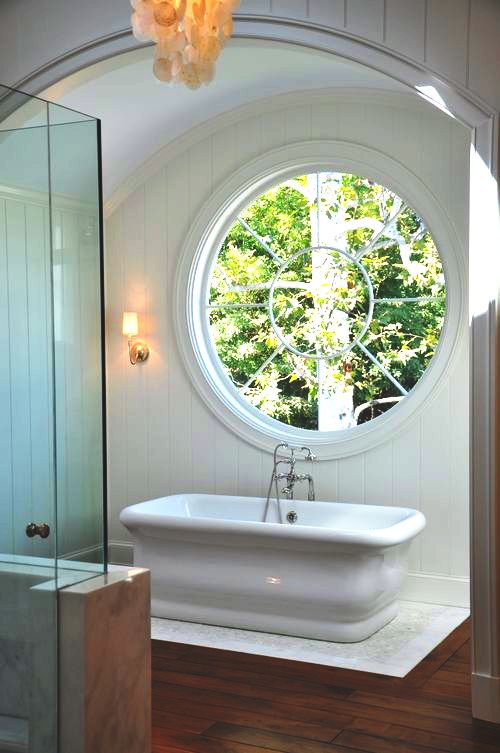 Freestanding composite tub under a large round window in a bathroom in a Malibu home
