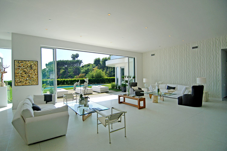 Living room in a modern Beverly Hills home by Meridith Baer & Associates with white tile floor, white walls and white upholstered furniture and natural wood and glass accents