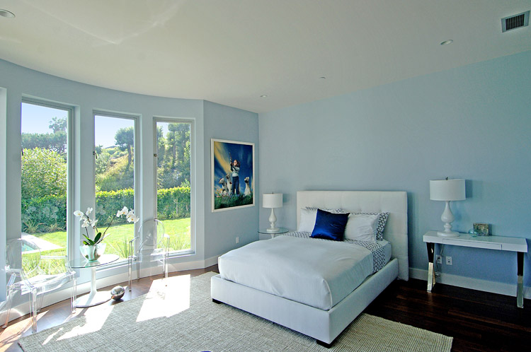 Bedroom with curved window wall, white upholstered bed, white table lamps and light blue walls in a modern Beverly Hills home by Meridith Baer & Associates