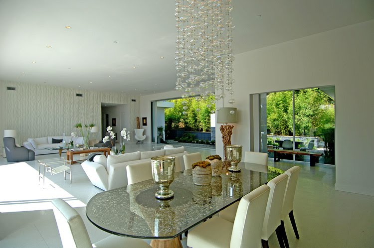 Light and airy formal dining room in a modern Beverly Hills home by Meridith Baer & Associates with a textured glass oval table, bubble glass chandelier, white upholstered dining chairs and silver urns
