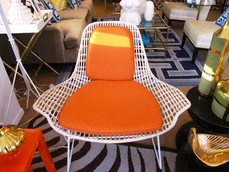 Modern woven white rattan chair on white metal frame with orange seat cushions in the Jonathan Adler store