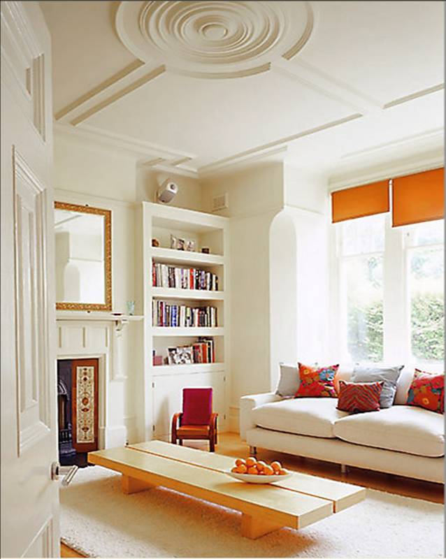 Living room with high ceilings with modern round ceiling medallion, cream walls, built in bookshelf and sofa with orange curtains