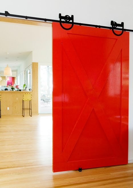 Red interior barn door slides on black metal exposed hardware leading to a kitchen by Bestor Architecture