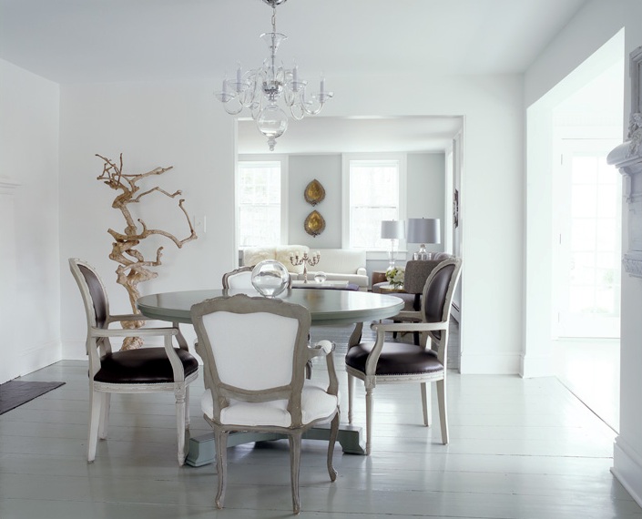 White dining room with driftwood sculpture, glass chandelier, round pedestal dining table and upholstered reproductions of Louis XVI chair