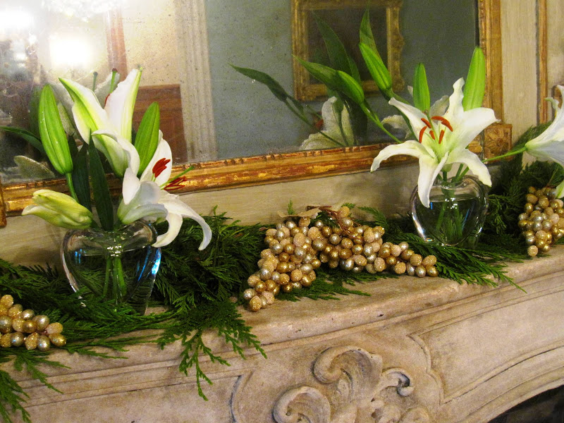 Fireplace in the ladies parlor of a historic New Orleans mansion with a garland made of a cedar/pine bows, faux frosted gold grapes, star gazer lilies in simple clear vases and gold candlesticks