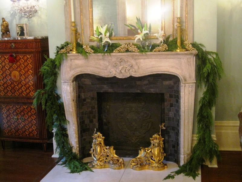 Fireplace in the ladies parlor of a historic New Orleans mansion with a garland made of a cedar/pine bows, faux frosted gold grapes, star gazer lilies in simple clear vases and gold candlesticks