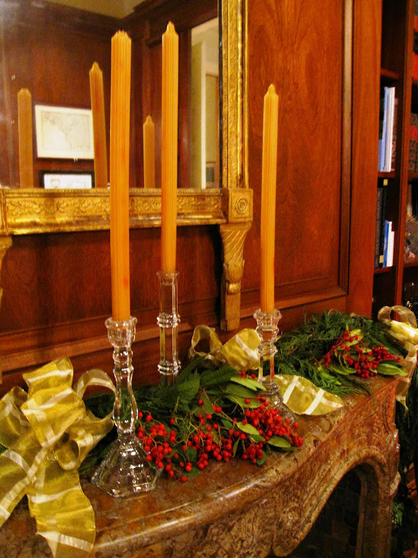 Fireplace in the library of a historic New Orleans mansion with a garland made of cedar boughs, red eucalyptus berries, crystal candle sticks and gold ribbon