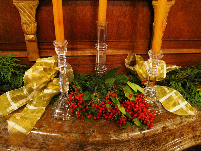 Fireplace in the library of a historic New Orleans mansion with a garland made of cedar boughs, red eucalyptus berries, crystal candle sticks and gold ribbon