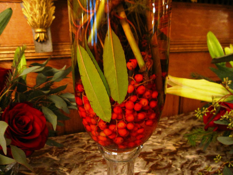 Close up of the base of a flower arrangement of white star gazer lilies, pine tree branches, eucalyptus leaves, red berries and a touch of red food coloring in the main entry hall in a New Orleans mansion