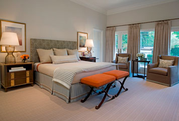 Bedroom by Massucco Warner Miller with orange x-benches at the foot of the bed, grey armchairs, curtains and upholstered headboard