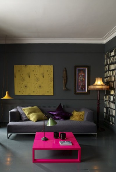 Dark grey living room with grey floor, built in bookshelf, grey sofa, a yellow lamp and a hot pink coffee table