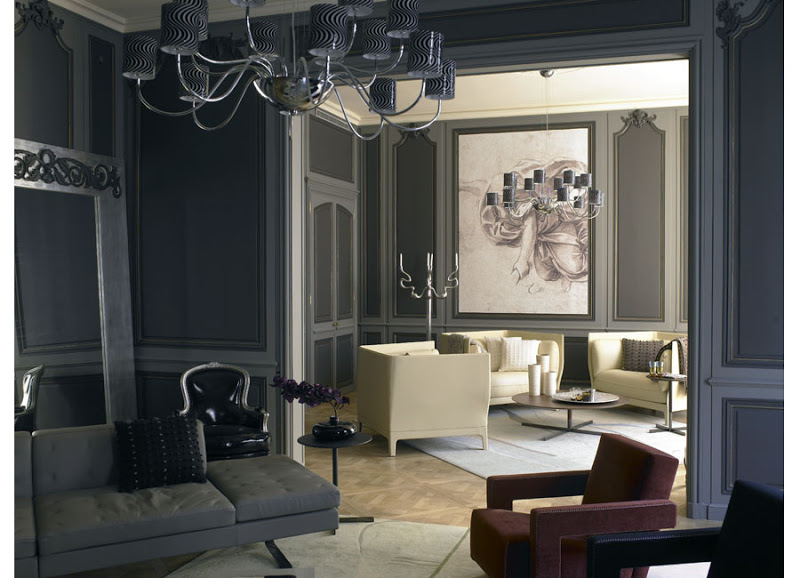 Dark grey living room with chandelier, wood paneled details, a grey sofa, red and black armchairs and herringbone wood floor