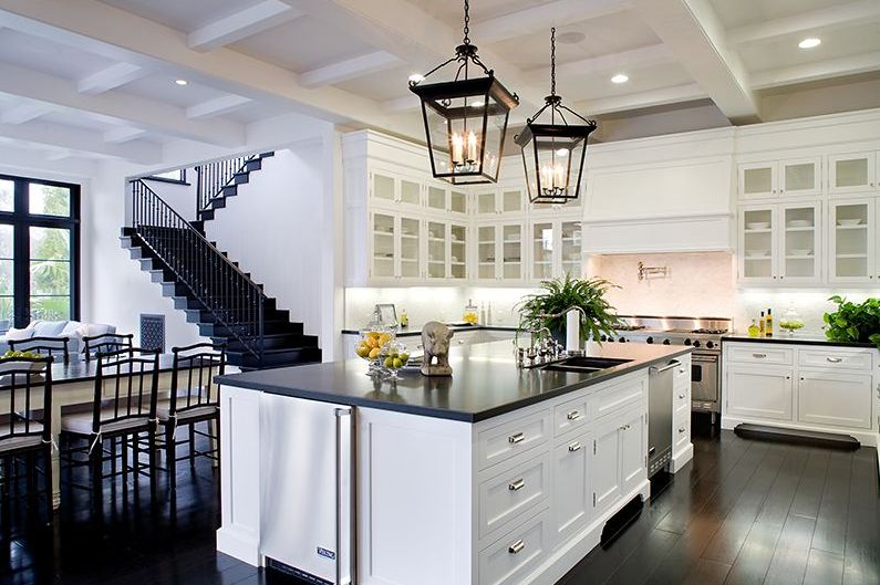 Eat in kitchen in a Spanish revival home with two lantern lights, white cabinets with glass fronts, coffered ceiling, and a white island with black countertops