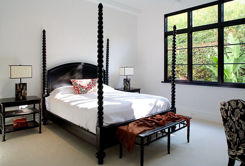 Bedroom in a Spanish revival home with black canopy bed, nightstand and bench and black paned windows