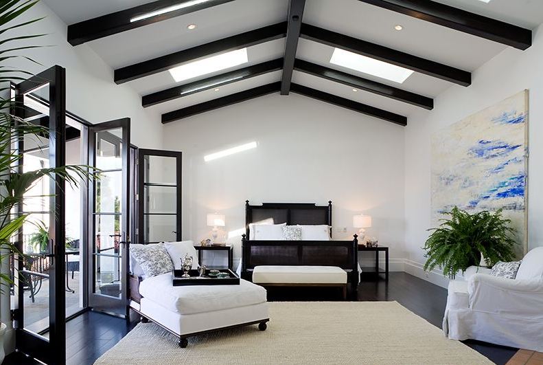 Master bedroom in a Spanish Revival home with exposed painted black beams and black glass doors opening up to a patio