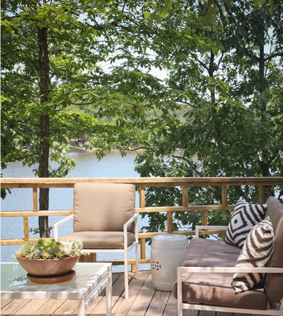 Outdoor patio with white iron furniture, diamond ikat style pillows, white ceramic garden stools and a lake view