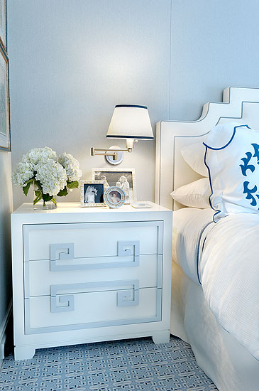 White nightstand in a master bedroom with white headboard and blue graphic print carpet
